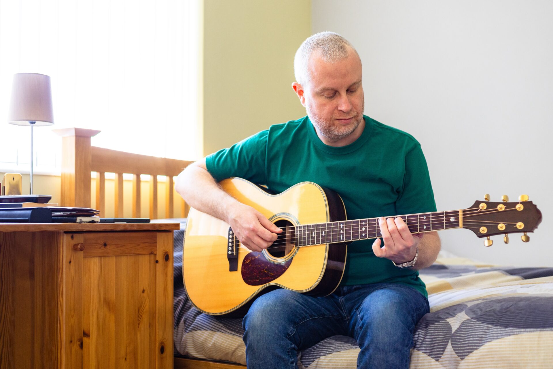 A person sitting on a bed, playing a guitar