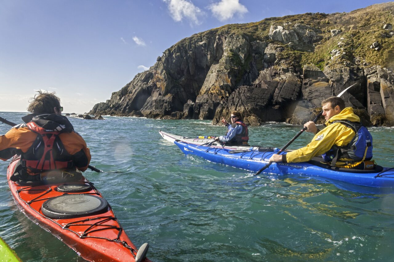Three people kayaking next to a mountain
