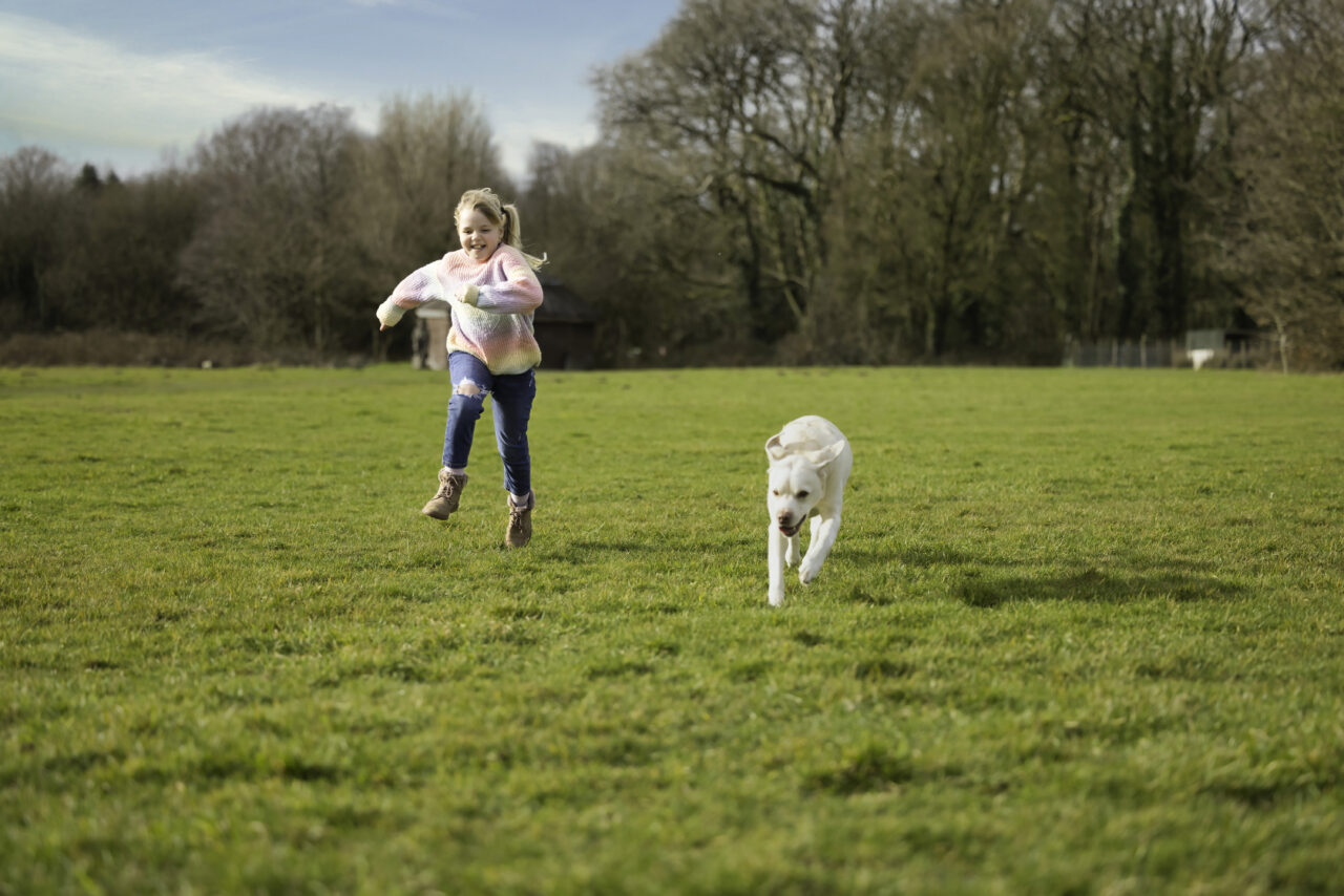 A young girl running outside with her dog.