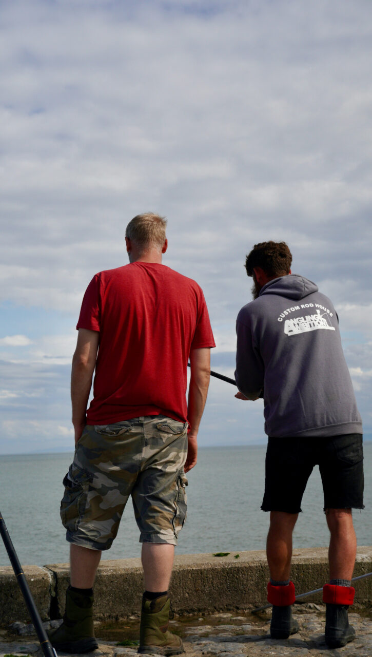 Two people fish at the edge of a sea wall
