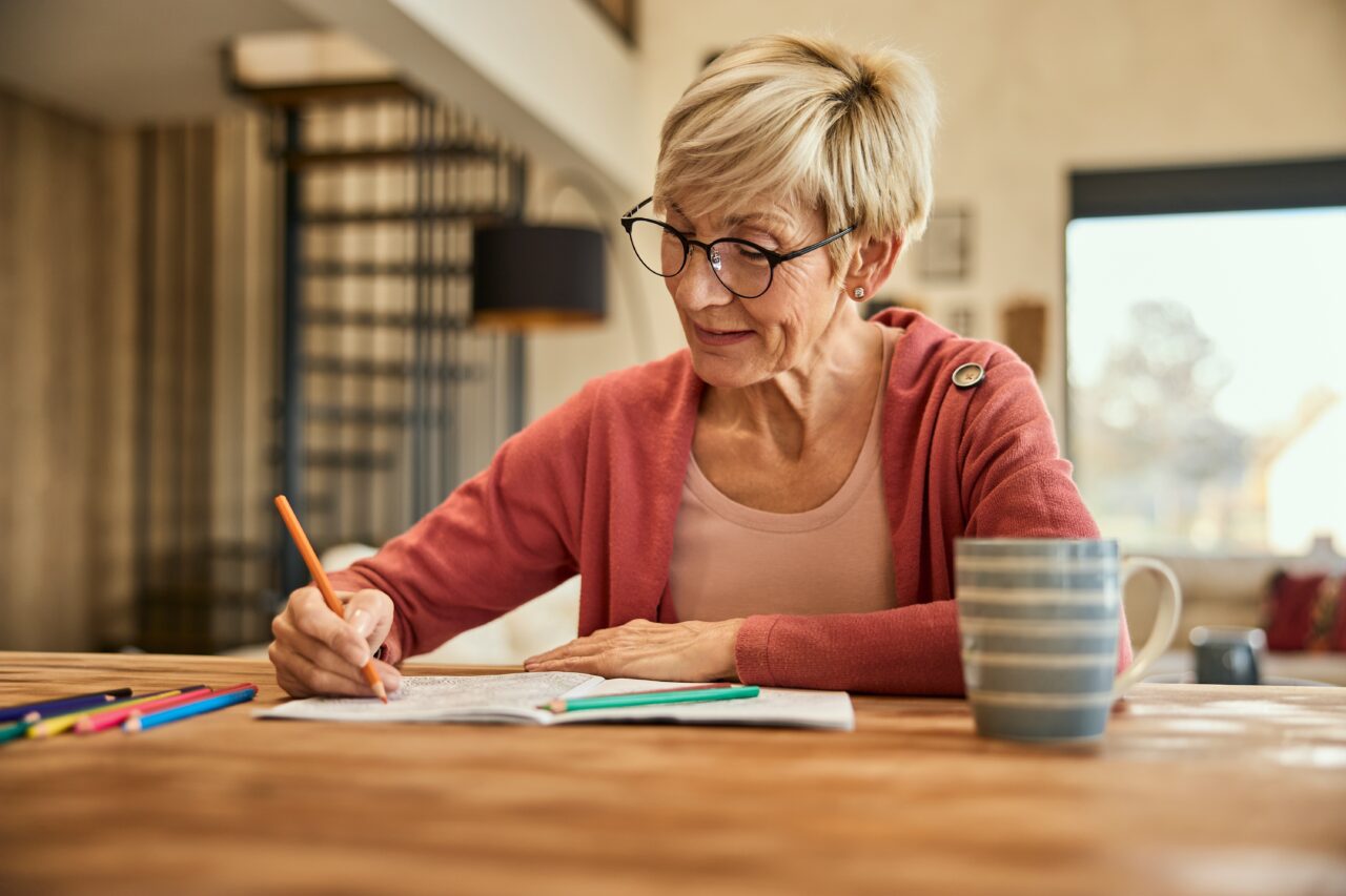 A woman sat at a table using coloured pencils in a colouring in book