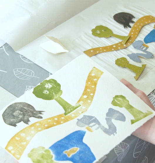 Darn o bapur gyda gwahanol brintiau wedi'i stampio arno: coeden, llwybr melyn, llyn, pysgodyn melyn a gwiwer. Wrth ei ymyl, ar ddalen arall o bapur, mae'r toriadau sy'n cyfateb i'r printiau. 