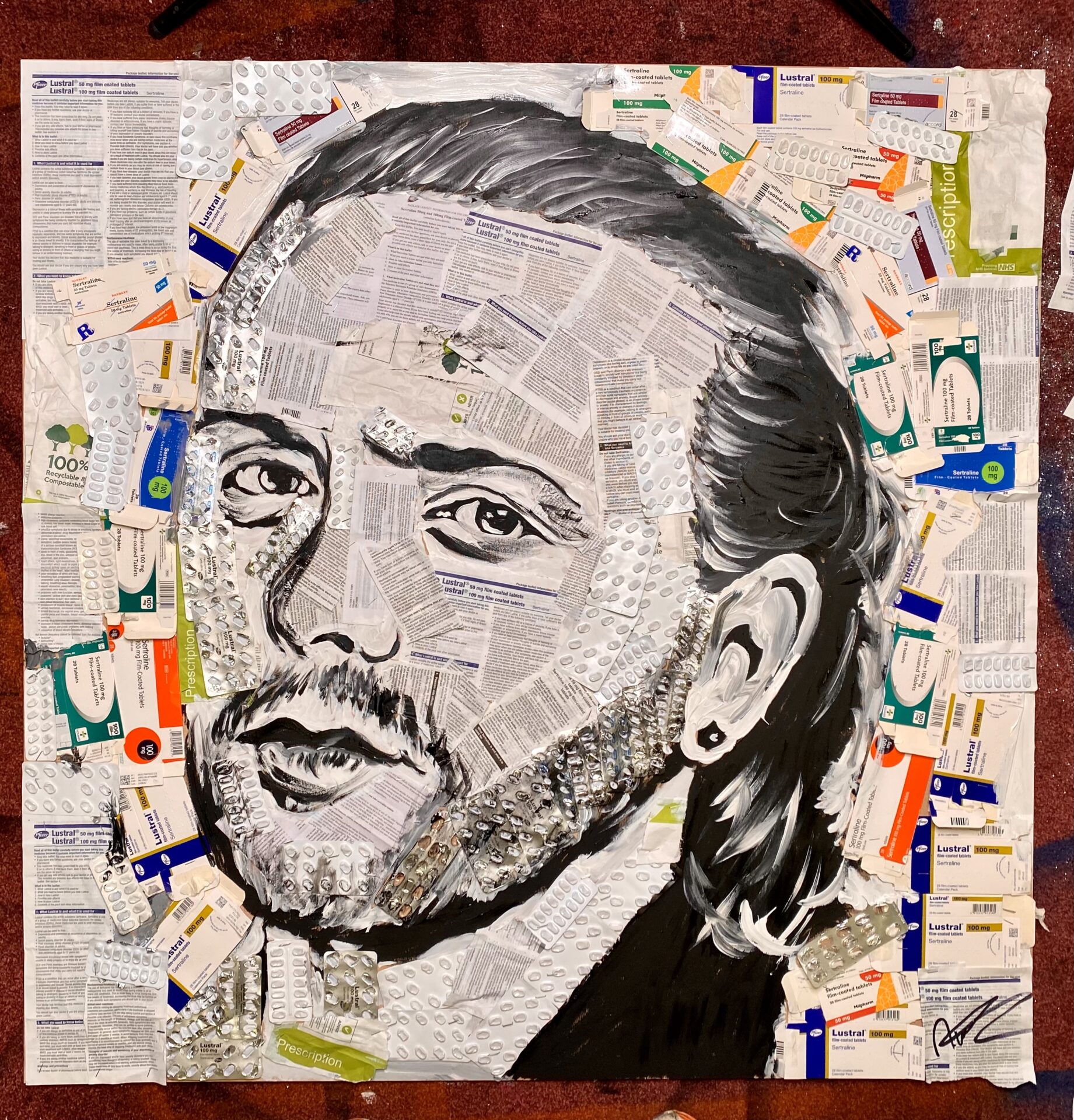 Portread o berson â barf a gwallt tywyll wedi'i gribo yn ôl. Mae'r portread wedi'i wneud â phin marcio du a hen becynnau presgripsiwn. 